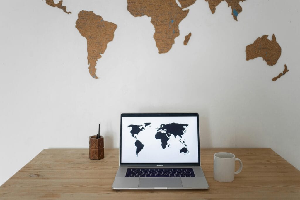 pexels-photo-7411982-7411982 Black world map on laptop screen and ceramic cup with pen container placed on table against silhouettes of continents