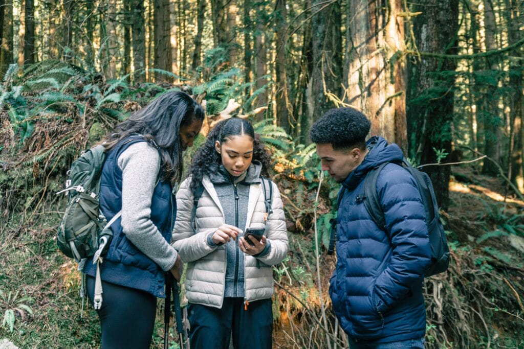 pexels-photo-7625220-7625220 A group of young hikers standing in the forest using a smartphone for navigation.